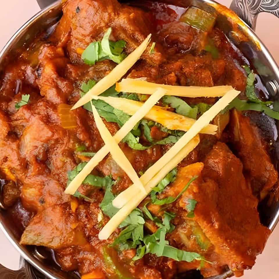 Close-up of a vibrant Indian curry, garnished with fresh cilantro and ginger slivers, in a metal bowl.