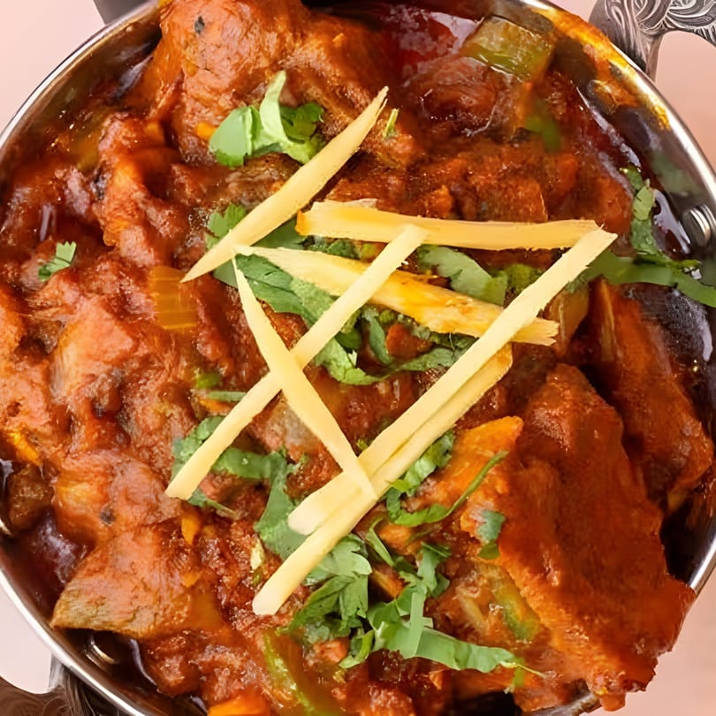Close-up of a vibrant Indian curry, garnished with fresh cilantro and ginger slivers, in a metal bowl.