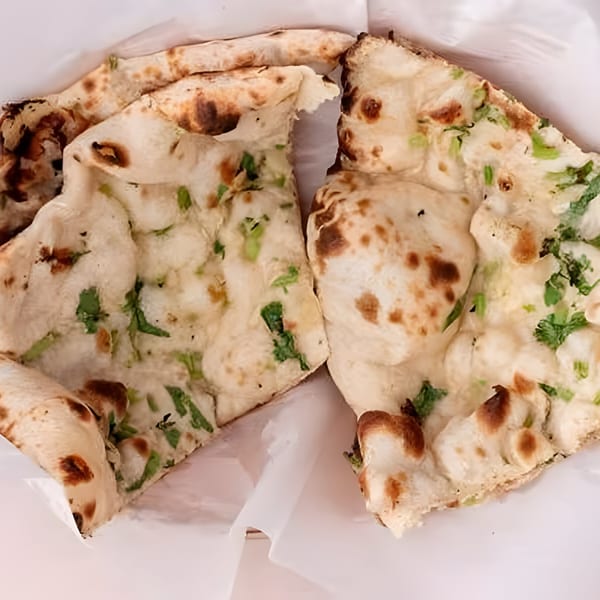 Two pieces of fresh, warm Indian naan bread, speckled with green herbs and browned spots.