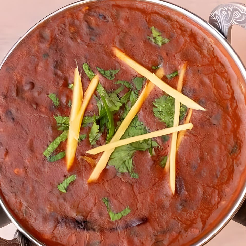 Close-up of a rich, dark red Indian curry, garnished with fresh cilantro and ginger strips.