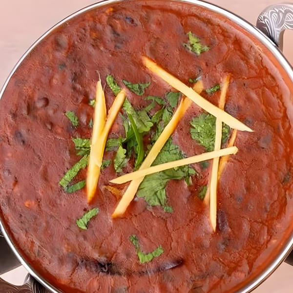 Close-up of a rich, dark red Indian curry, garnished with fresh green herbs and thin ginger strips.