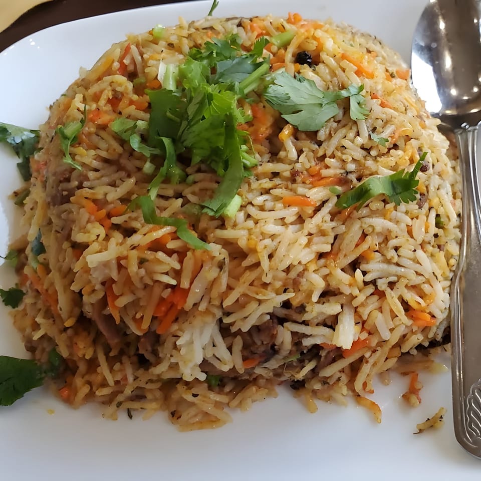 A large serving of Indian biryani rice with carrots and cilantro on a white plate with a spoon.